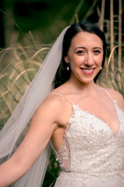 Bride smiles in grass setting wearing veil